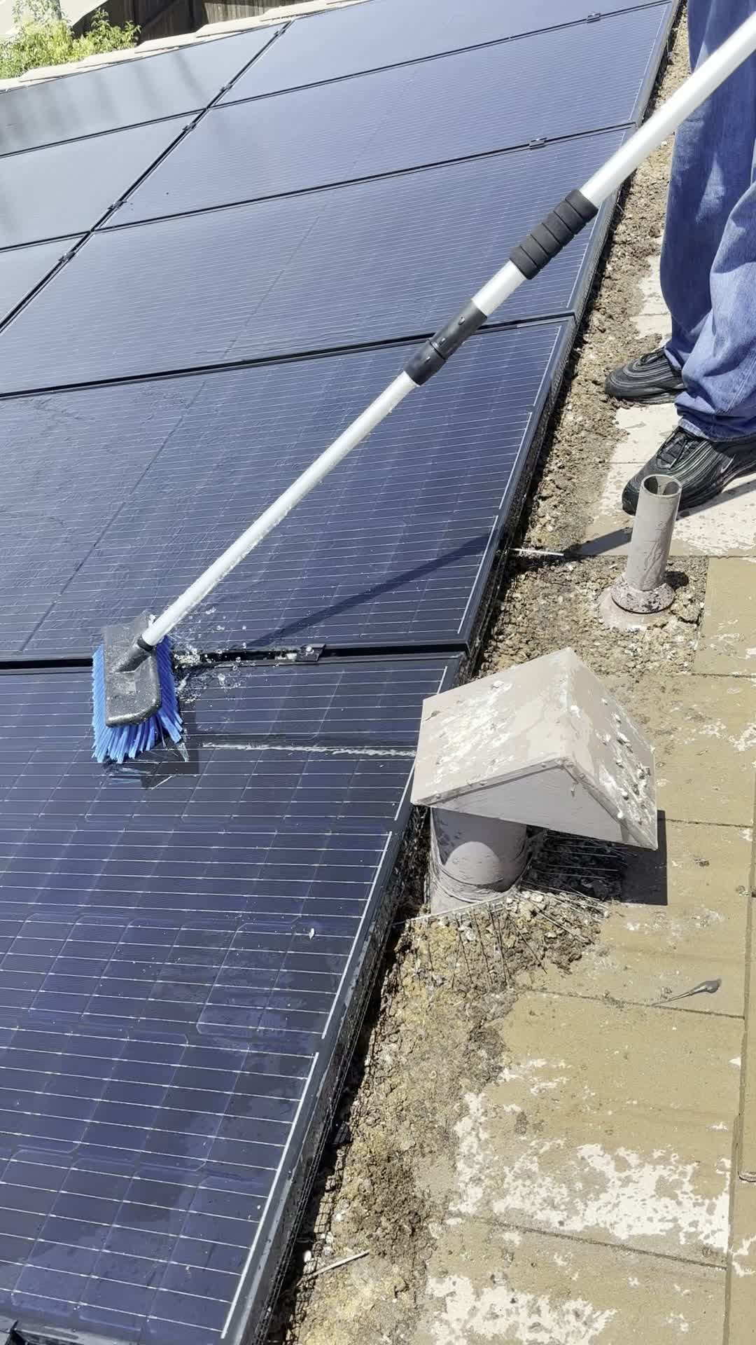 Valley Concrete technician using a soft-bristle brush pole and water to gently clean a rooftop solar panel up close.