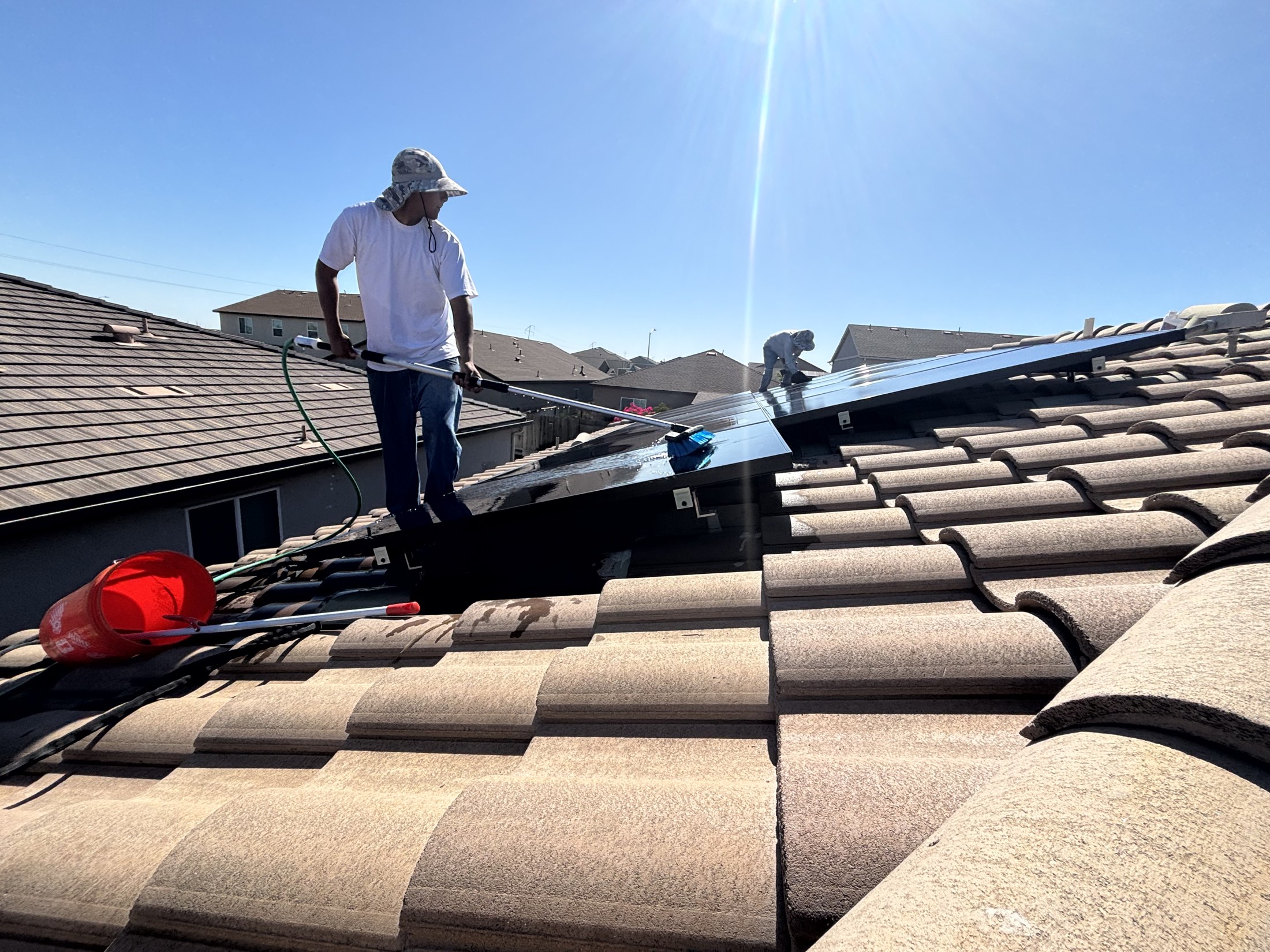 Valley Concrete technician standing on a tile roof beside a rooftop solar array on a bright sunny day.