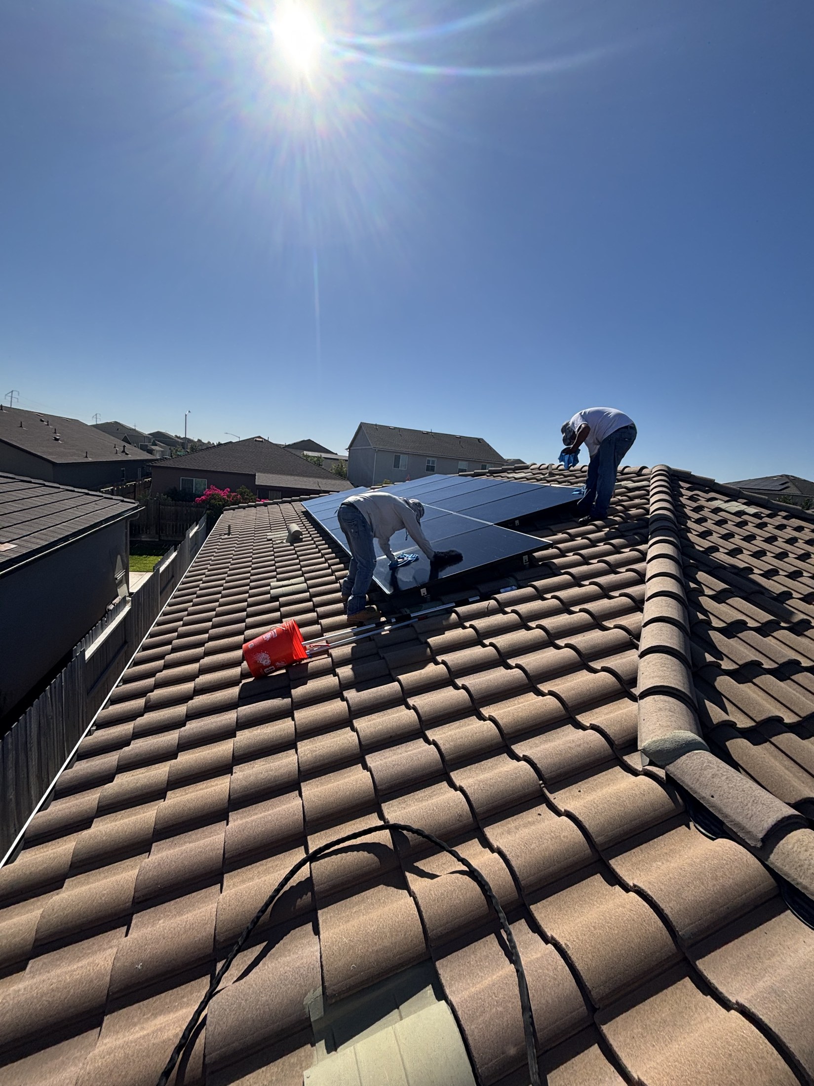 Technician kneeling on a roof carefully soft-washing residential solar panels.
