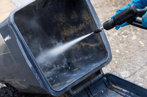 Technician pressure washing the inside of a dirty trash bin, blasting away built-up grime and odor.